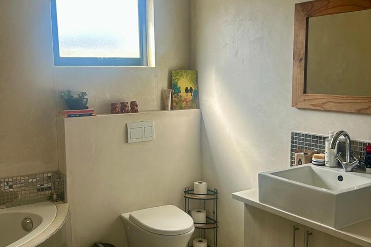 A functional bathroom featuring a wall-hung toilet, corner bathtub, and a modern vessel sink vanity with mosaic tile accents.