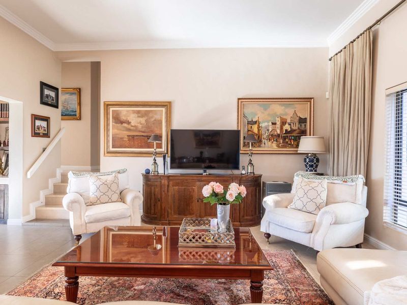 A well-maintained living room featuring crown molding, tiled flooring, and a staircase leading to an adjacent built-in shelving area.