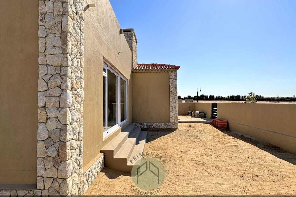 Rear exterior view of the property featuring stone-clad accents, sliding glass doors, and an expansive, undeveloped backyard area.