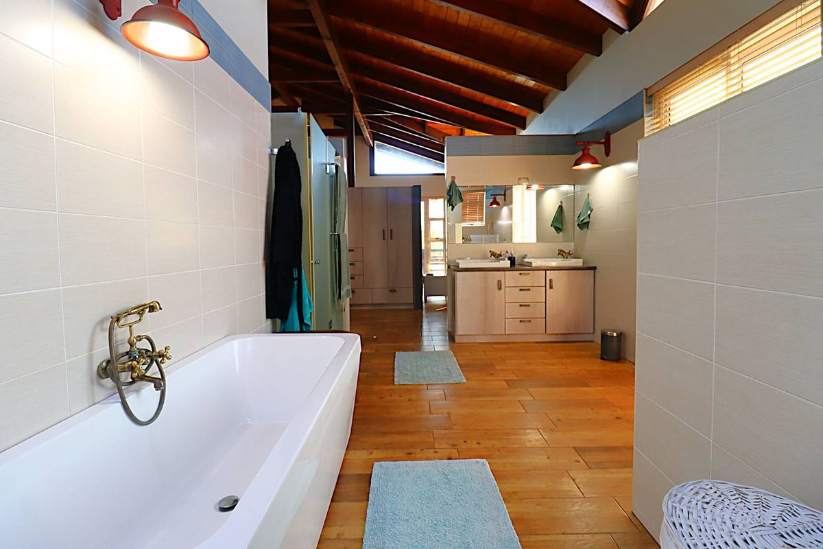 Spacious bathroom featuring a freestanding bathtub, double vanity with integrated sinks, timber flooring, and exposed wooden ceiling beams.