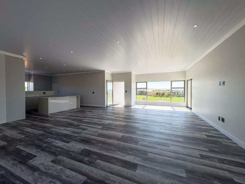 Spacious open-plan living and kitchen area featuring modern laminate flooring, recessed lighting, and large windows with scenic views.