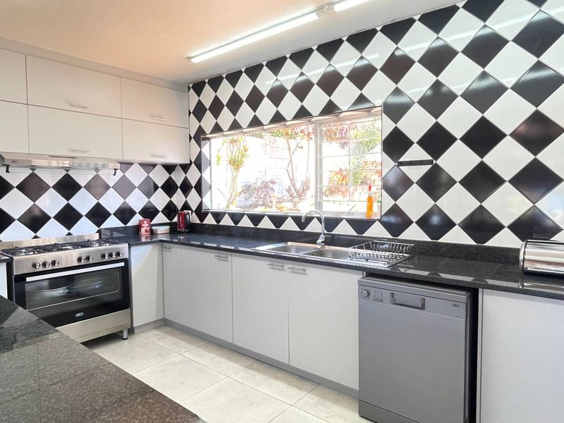 A functional kitchen featuring white cabinetry, granite countertops, a gas stove, and a distinctive black and white diamond-patterned tiled backsplash.