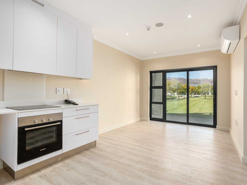 Modern open-plan kitchen and living area featuring sleek white cabinetry, integrated appliances, and large sliding doors opening to a landscaped garden view.