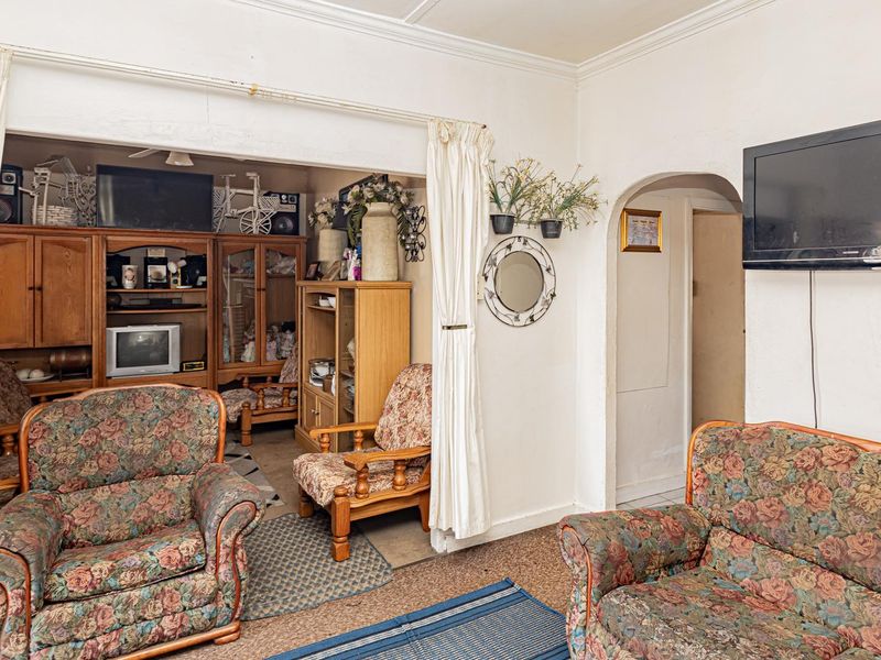 A living room area featuring a classic archway and traditional ceiling cornicing, offering a functional layout with potential for cosmetic updates.