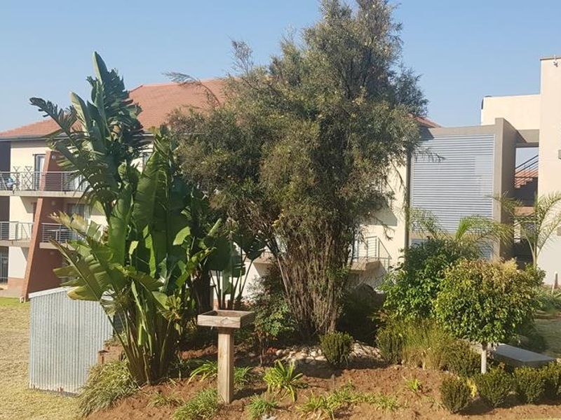 Rear view of the apartment complex featuring landscaped garden areas, paved pathways, and private balconies with metal privacy screens.