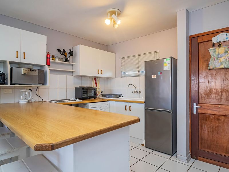 Compact kitchen featuring white cabinetry, a wooden breakfast bar, tiled flooring, and a classic timber door, offering a functional layout for an apartment.