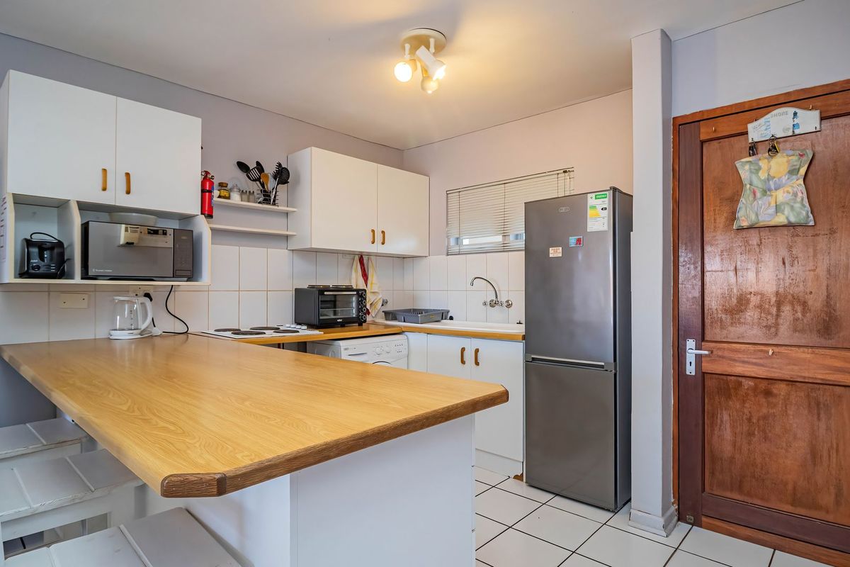 Compact kitchen featuring white cabinetry, a wooden breakfast bar, tiled flooring, and a classic timber door, offering a functional layout for an apartment.