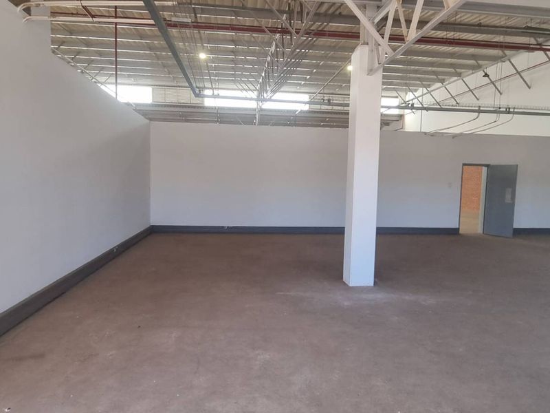 Spacious industrial utility area featuring exposed steel roof trusses, concrete flooring, and integrated fire safety systems, suitable for various commercial or storage applications.