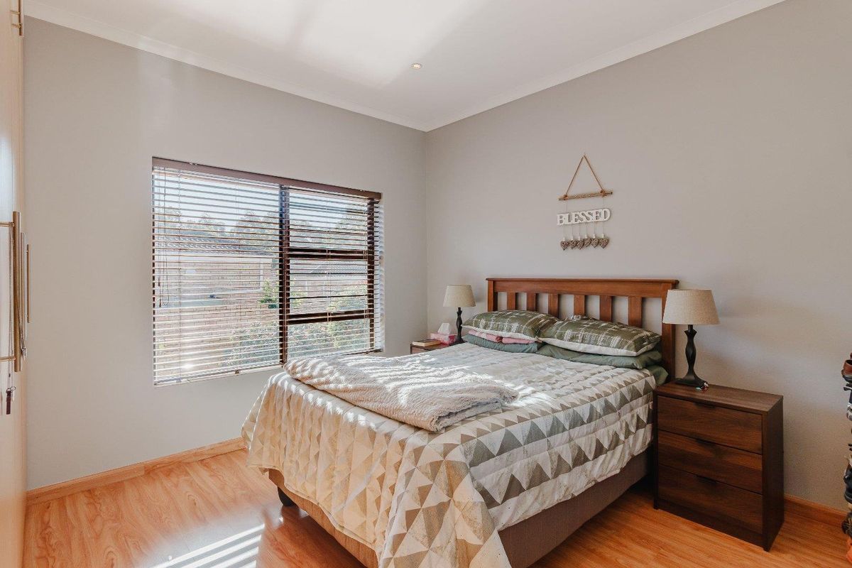 A well-maintained bedroom featuring light-toned laminate flooring, neutral wall finishes, and a large window fitted with horizontal blinds.