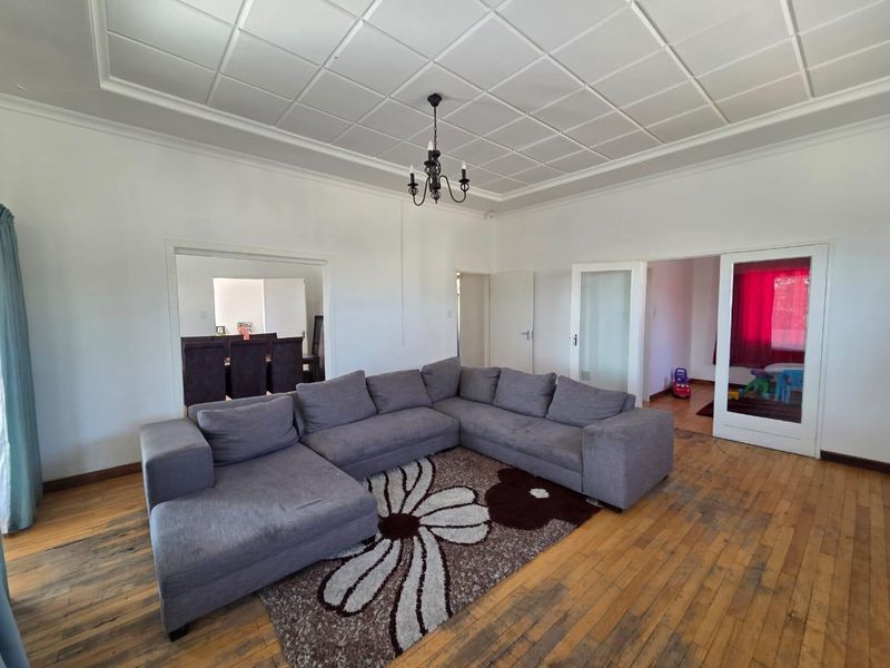 Spacious living room featuring original hardwood flooring, a decorative coffered ceiling, and classic chandelier lighting, with direct access to adjacent rooms.