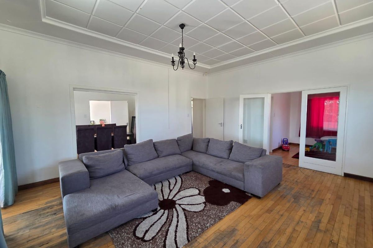 Spacious living room featuring original hardwood flooring, a decorative coffered ceiling, and classic chandelier lighting, with direct access to adjacent rooms.