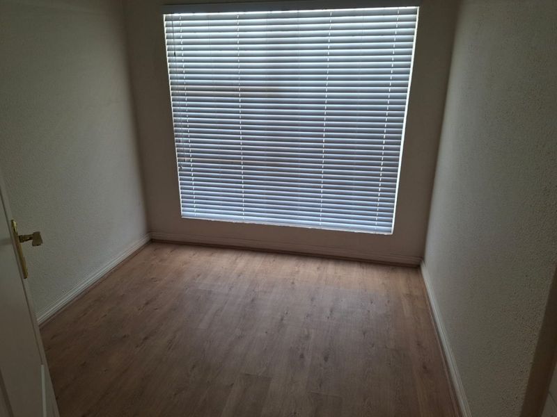 A clean, empty bedroom featuring light wood-look laminate flooring and fitted venetian blinds, providing a neutral canvas for personalization.
