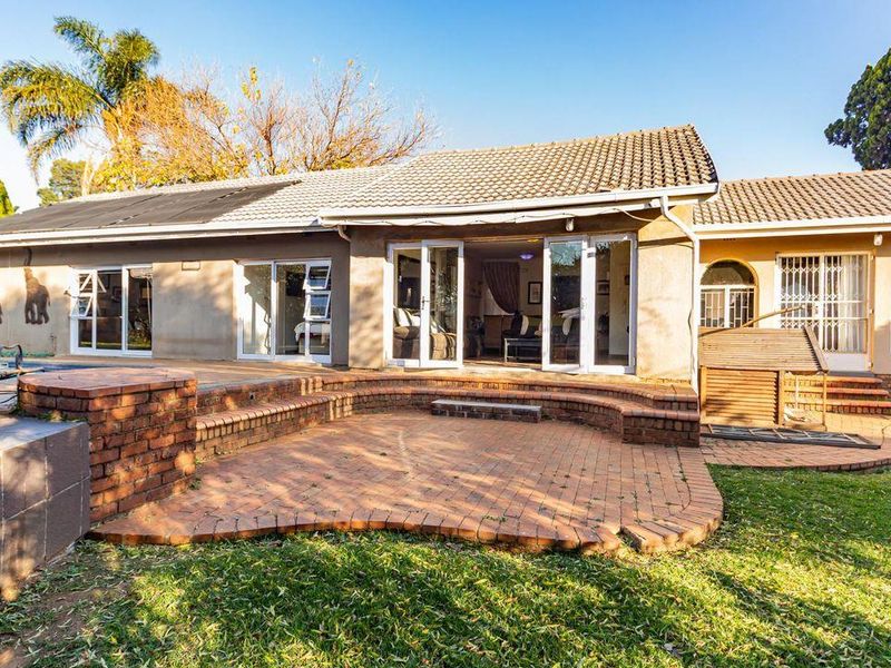 Rear view of the house featuring a brick-paved patio, sliding glass doors, and a well-maintained garden area.