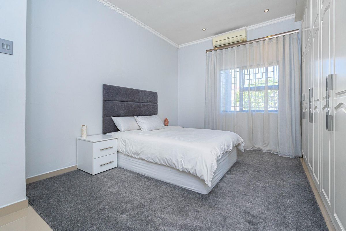 A well-maintained bedroom featuring plush grey carpeting, built-in floor-to-ceiling wardrobes, and a wall-mounted air conditioning unit.