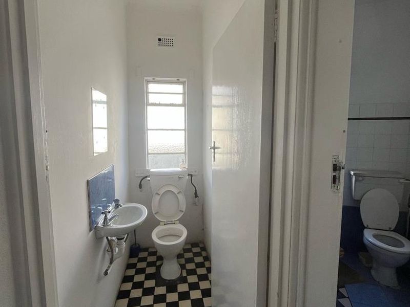 A small, dated bathroom featuring a wall-mounted basin, toilet, and classic checkerboard floor tiles, offering potential for a modern renovation.