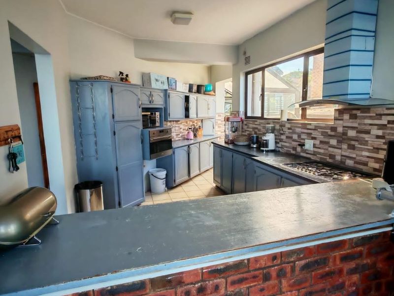 A functional kitchen featuring built-in cabinetry, a gas hob with extractor fan, tiled backsplash, and a brick-faced breakfast bar.