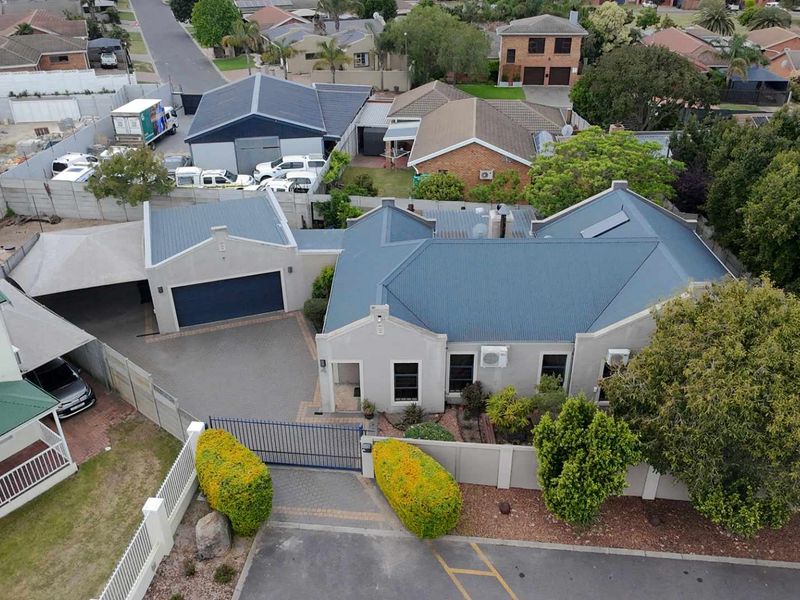Aerial view of a residential property featuring a corrugated metal roof, paved driveway, secure garage, and established garden boundaries.