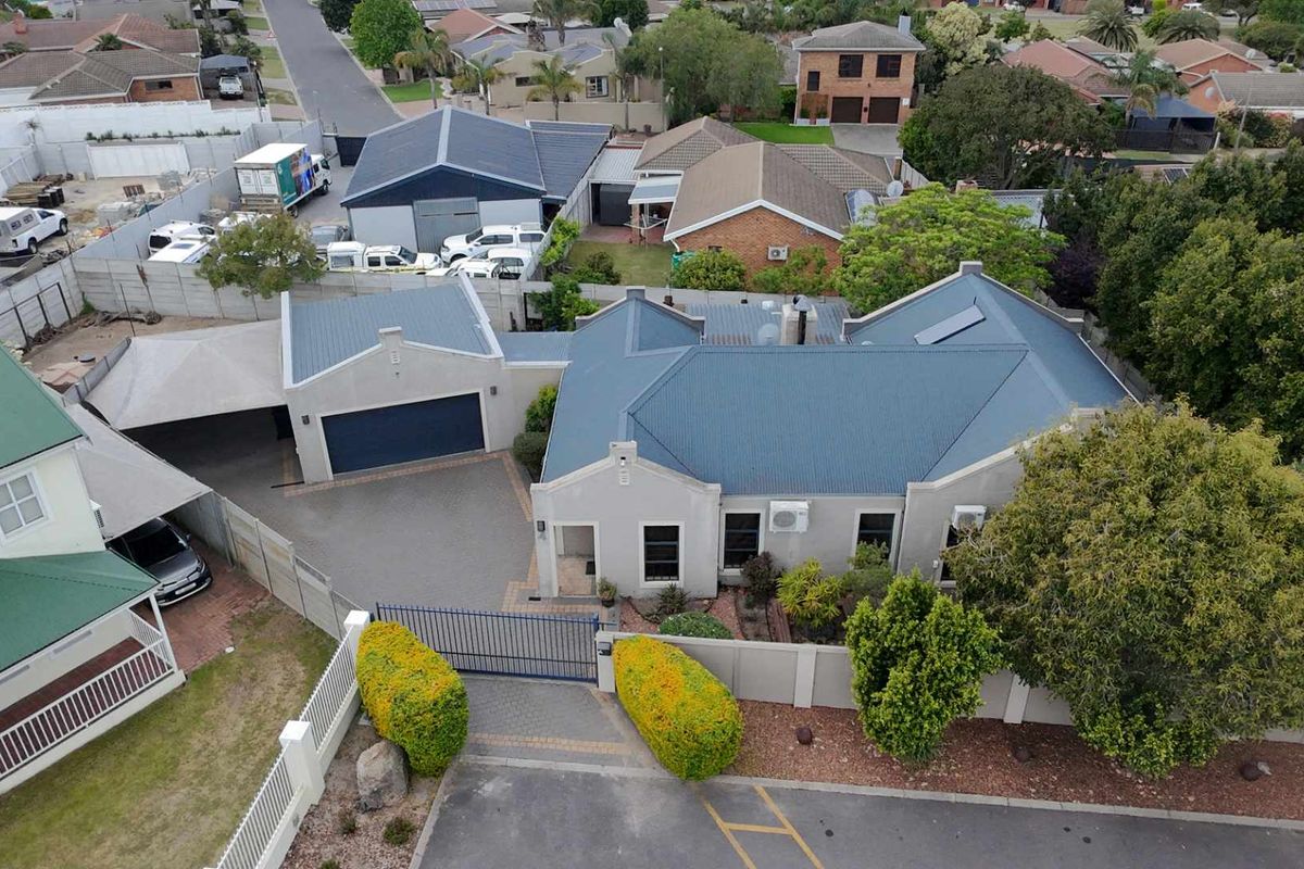 Aerial view of a residential property featuring a corrugated metal roof, paved driveway, secure garage, and established garden boundaries.
