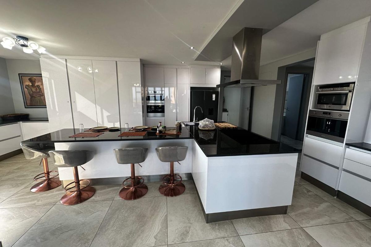 Modern kitchen featuring high-gloss white cabinetry, black granite countertops, a central island, and integrated stainless steel appliances with large format floor tiles.
