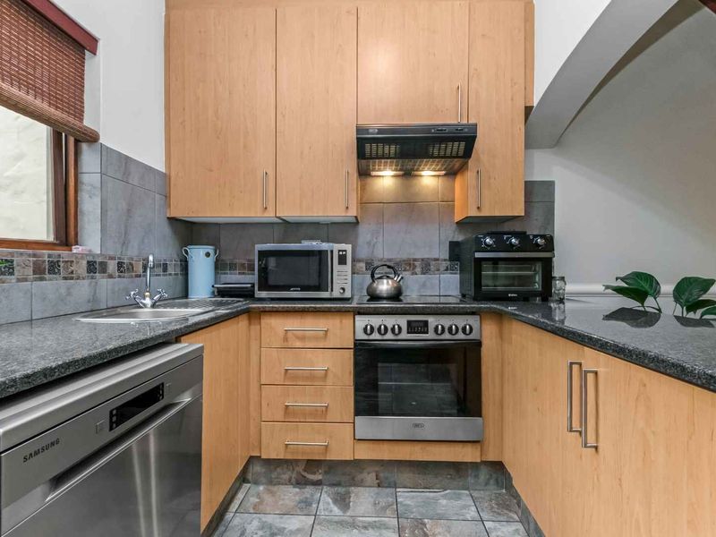 Compact kitchen featuring light wood cabinetry, granite countertops, tiled backsplash, and built-in oven with extractor fan.