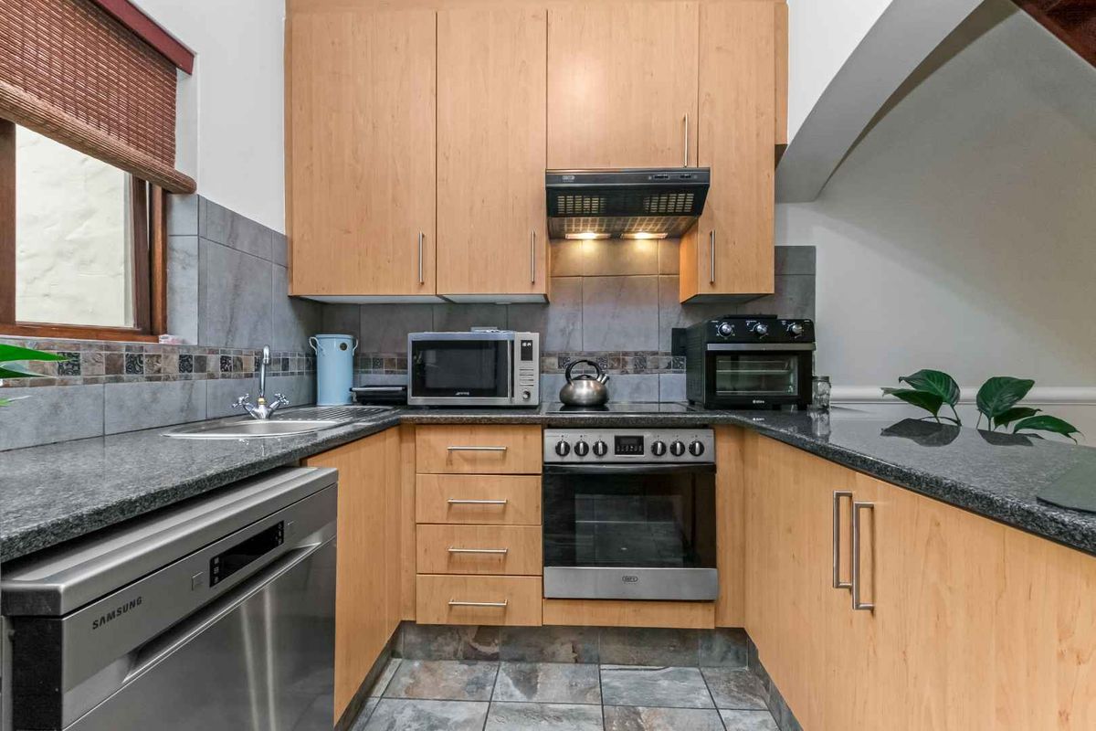 Compact kitchen featuring light wood cabinetry, granite countertops, tiled backsplash, and built-in oven with extractor fan.