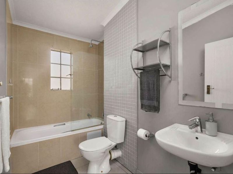 A clean and functional bathroom featuring a bathtub with a glass shower screen, a pedestal sink, and neutral wall tiling.