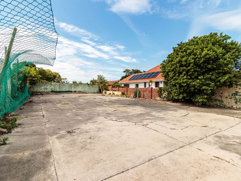 A spacious rear yard featuring extensive concrete paving, boundary walls, and a view of the main dwelling with roof-mounted solar panels.