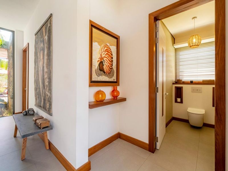 A bright hallway featuring modern tile flooring and timber door frames, leading into a compact, well-appointed bathroom with a wall-mounted toilet.