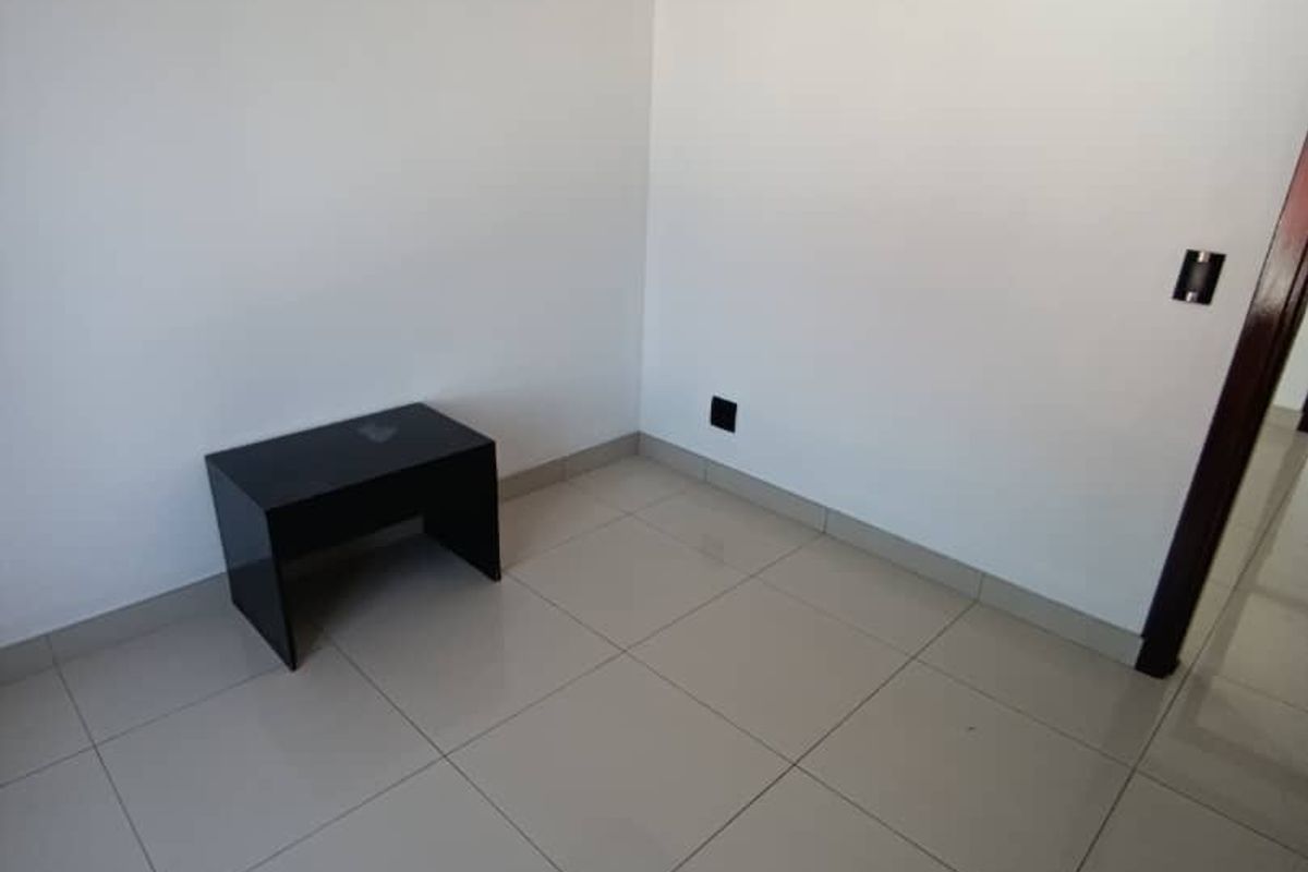 A clean, empty room featuring neutral tiled flooring, white walls, and dark wood trim detailing.