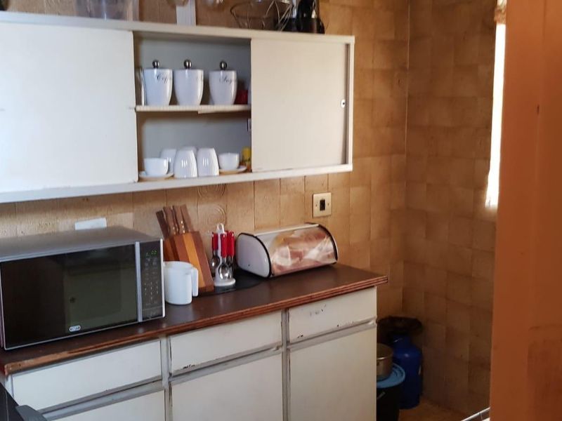 A compact kitchen area featuring dated wall tiles and original built-in cabinetry with laminate countertops, offering potential for a modern renovation.