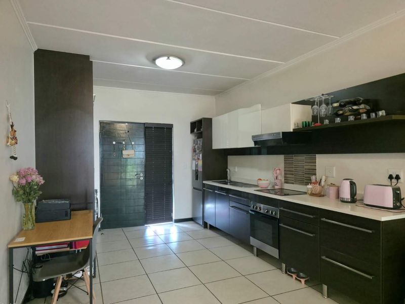 Modern kitchen featuring dark cabinetry, white countertops, built-in oven and hob, extractor fan, and tiled flooring with direct access to an exterior door.