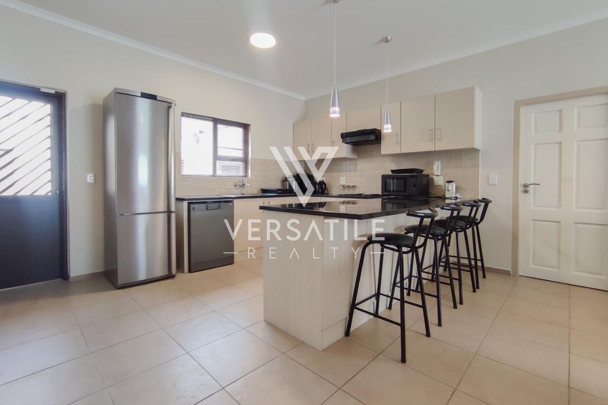 A functional kitchen featuring light-toned cabinetry, dark granite countertops, a central breakfast island, and tiled flooring.