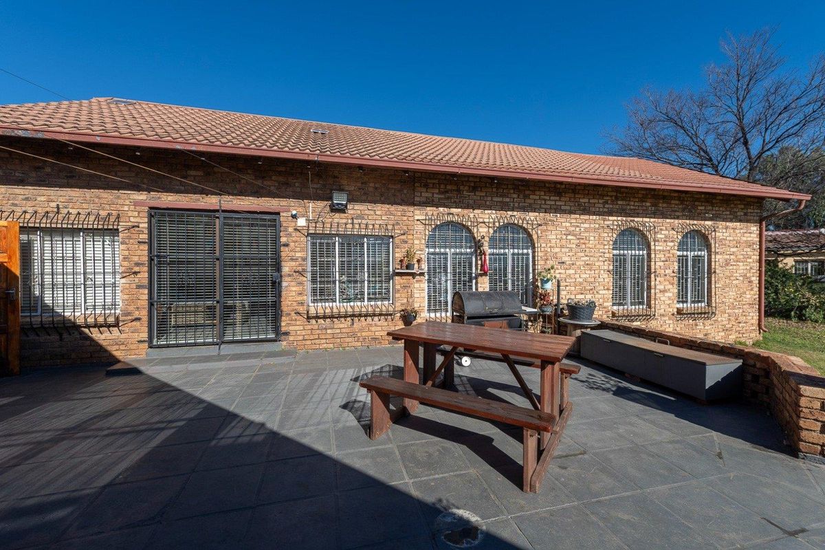 A spacious rear patio area featuring dark tiled flooring, brick exterior walls, and secure metal security gates and window bars.