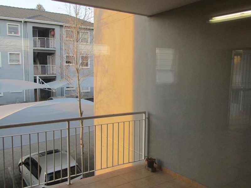 A covered balcony featuring tiled flooring and a metal balustrade, overlooking the apartment complex parking area.