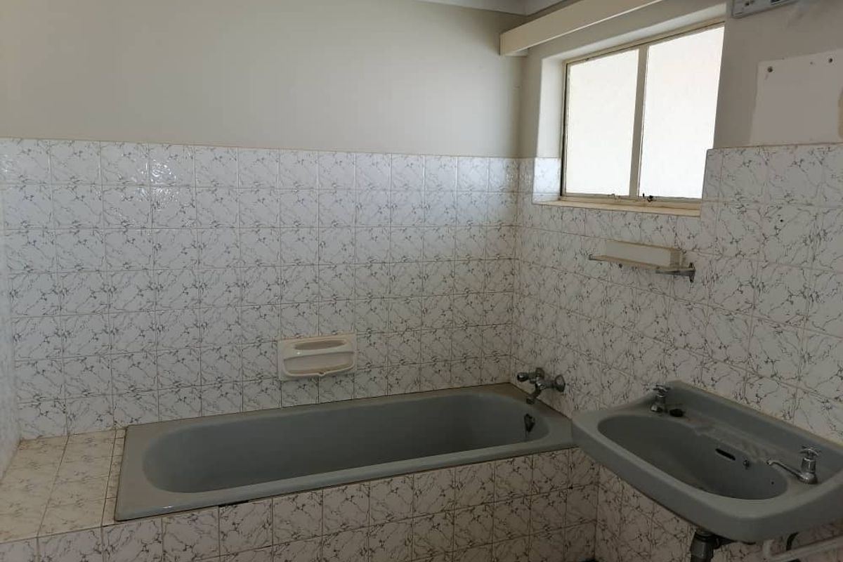 A dated bathroom featuring a built-in bathtub, wall-mounted basin, and patterned ceramic wall tiles.