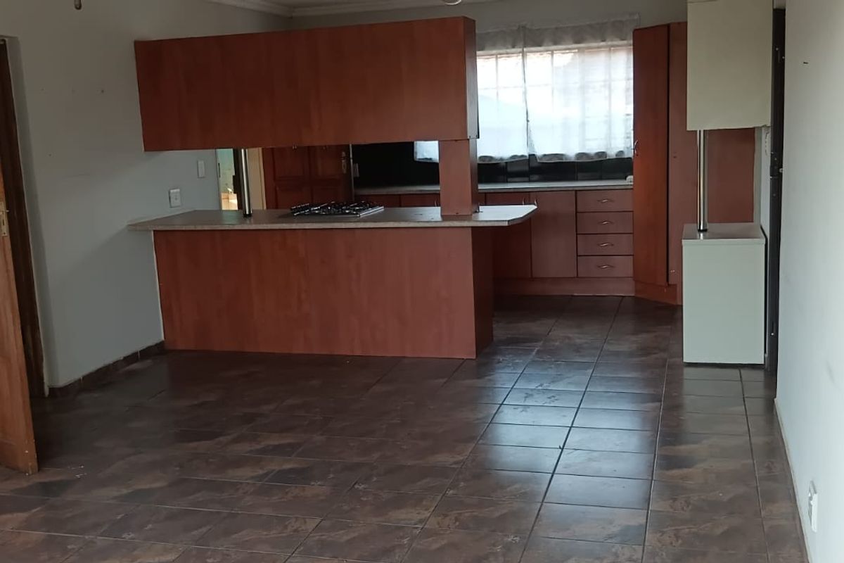 An empty kitchen featuring wooden cabinetry, laminate countertops, a built-in gas hob, and dark tiled flooring, offering a blank canvas for renovation.