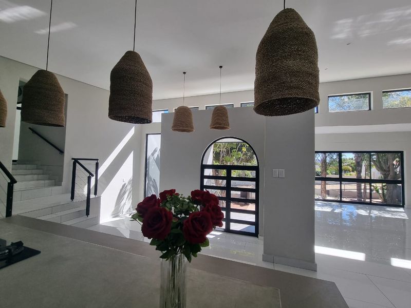 Spacious open-plan living area featuring high ceilings, modern arched entrance, sleek tiled flooring, and a contemporary staircase with integrated lighting.