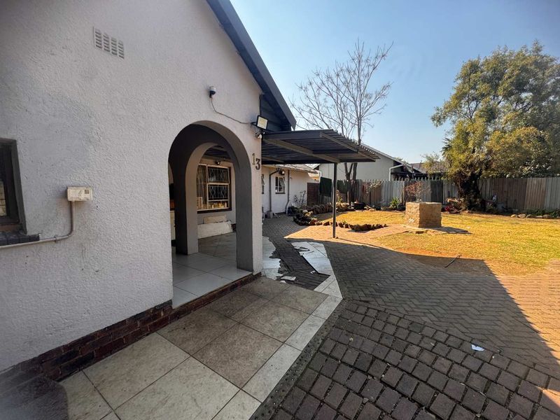 Rear exterior view featuring a covered patio area with arched entrance, paved garden space, and established landscaping.