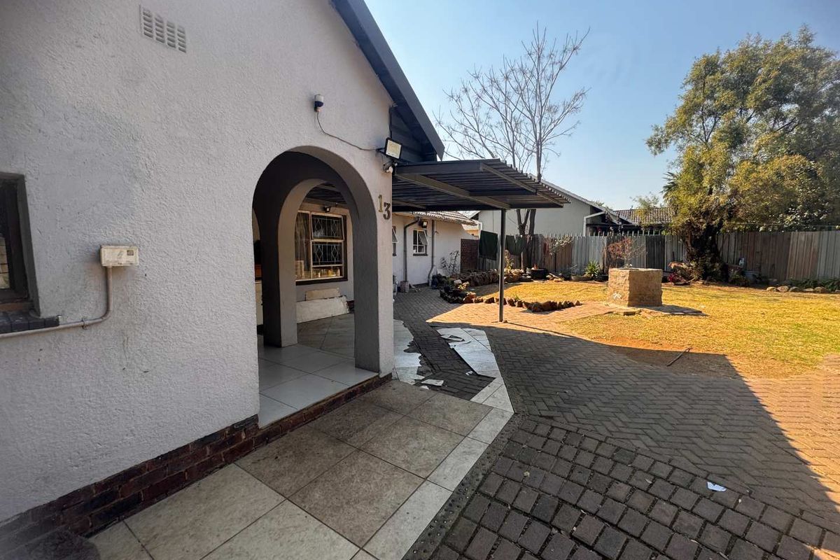 Rear exterior view featuring a covered patio area with arched entrance, paved garden space, and established landscaping.