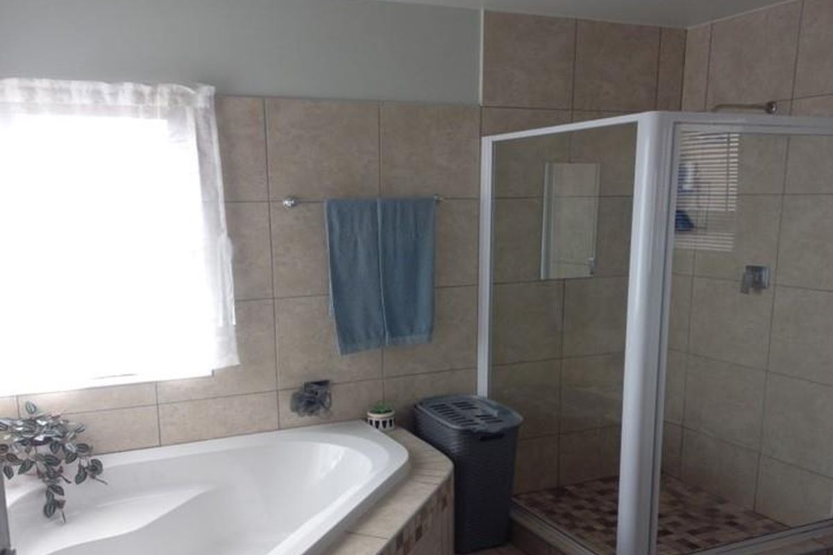A functional bathroom featuring a built-in corner bathtub, a separate glass-enclosed shower, and neutral wall tiling.