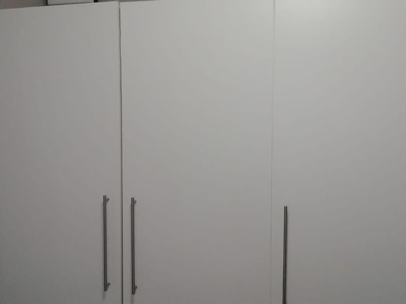 A bedroom featuring a modern, white built-in wardrobe with sleek metal handles.