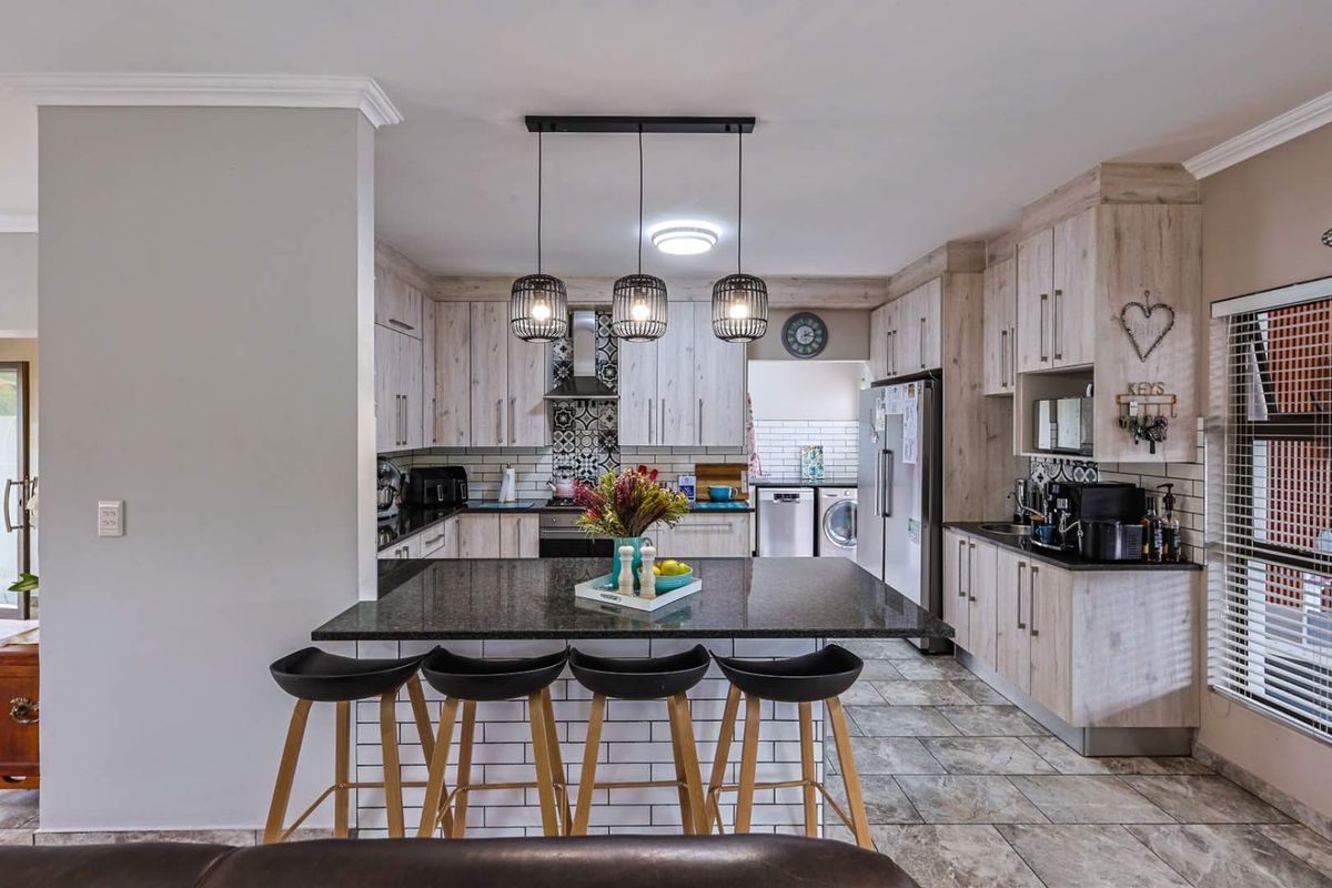 Modern kitchen featuring light wood-grain cabinetry, dark granite countertops, a central breakfast island, and a tiled backsplash with decorative accents.