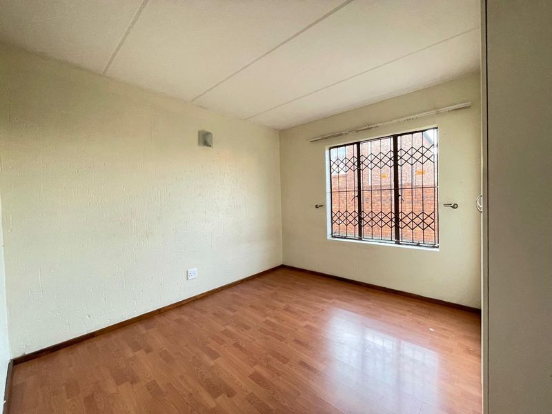 An empty bedroom featuring laminate flooring, a built-in cupboard, and a window fitted with a security gate.