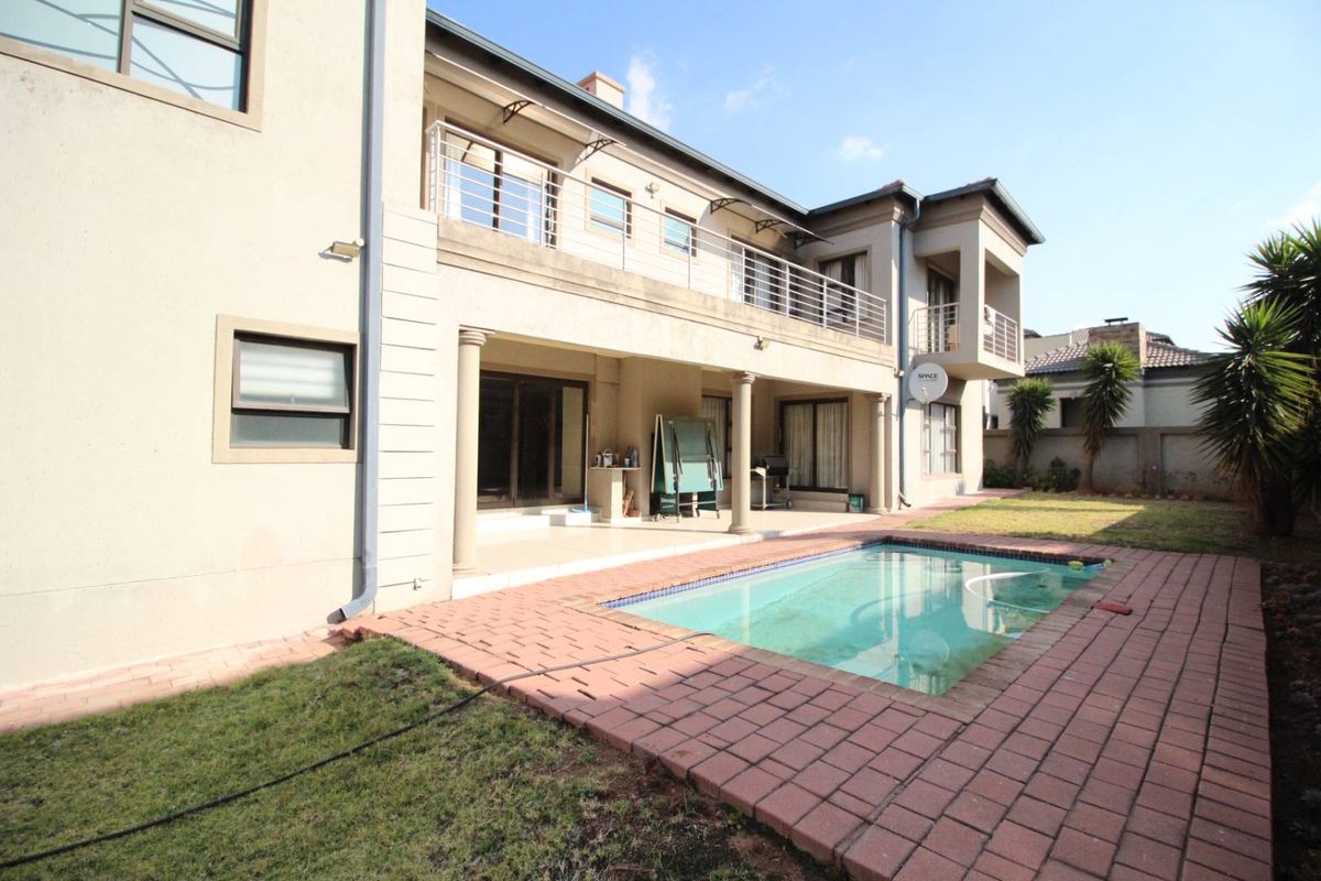 Rear view of the property featuring a covered patio, swimming pool with brick paving, and an upper-level balcony with metal railings.