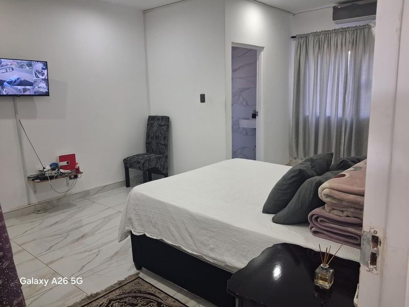 A bedroom featuring marble-look tiled flooring, an en-suite bathroom, and a wall-mounted air conditioning unit.