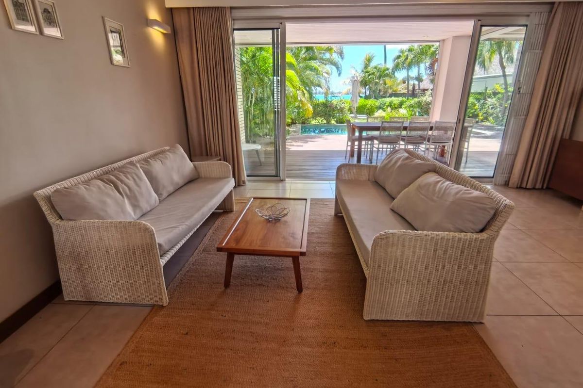 Spacious living area featuring large sliding glass doors that open onto a covered patio, swimming pool, and lush garden views.