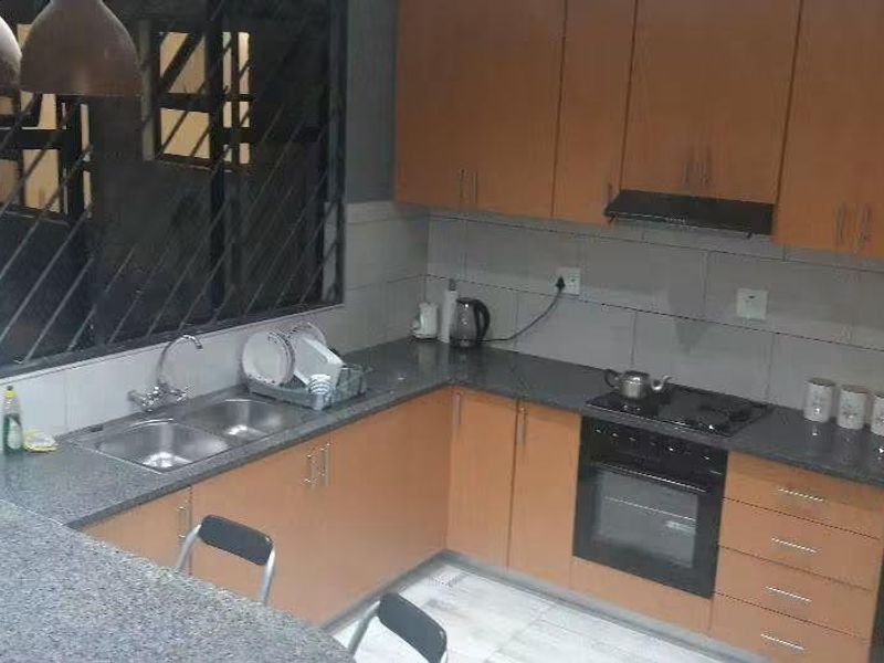 A functional kitchen featuring wooden cabinetry, granite countertops, a double basin sink, and integrated cooking appliances with a tiled backsplash.