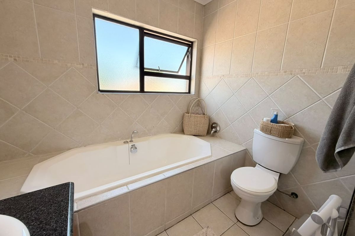 A functional bathroom featuring a built-in bathtub, toilet, and neutral tiled finishes throughout, providing a clean and practical space.