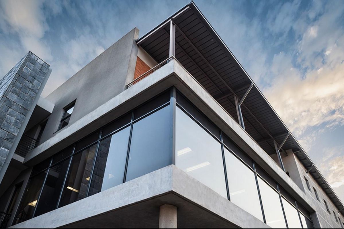 Modern office building exterior featuring a prominent glass curtain wall, stone cladding, and a covered upper-level balcony.