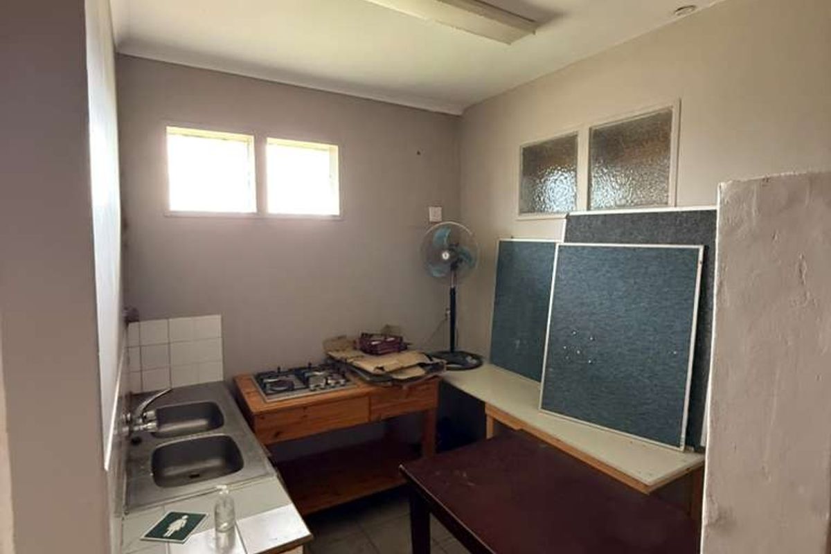 A functional industrial kitchen space featuring a stainless steel sink, built-in hob, and tiled flooring, requiring cosmetic updates to improve its overall condition.